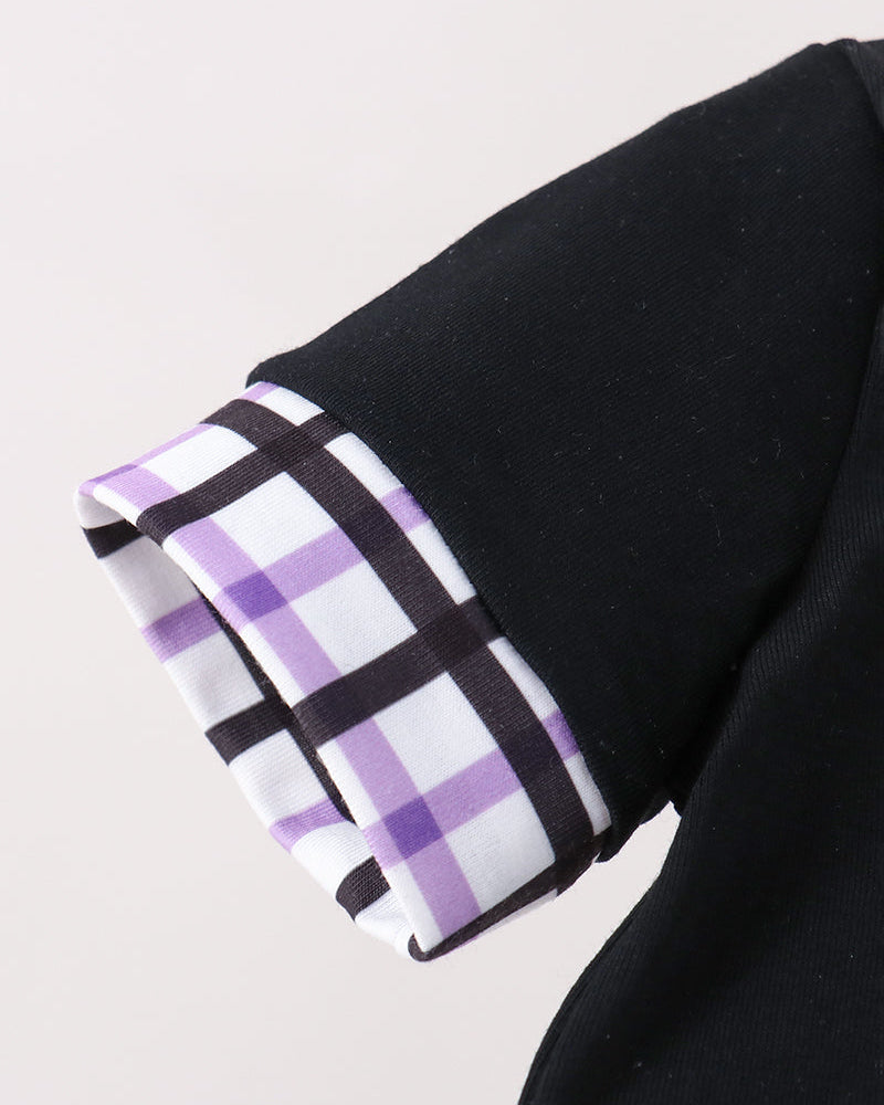 Close-up of a black garment sleeve with a folded cuff showing a purple, white, and black plaid lining pattern, set against a light gray background.