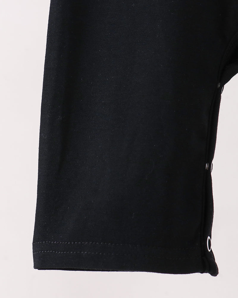 Close-up of a black garment romper leg with a hemmed edge and a small white circular detail near the lower side, shown against a plain light background.