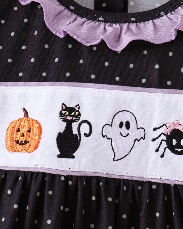 Close-up of a black and white polka dot dress with a lavender ruffled collar and a white horizontal band featuring embroidered Halloween motifs: a jack-o&