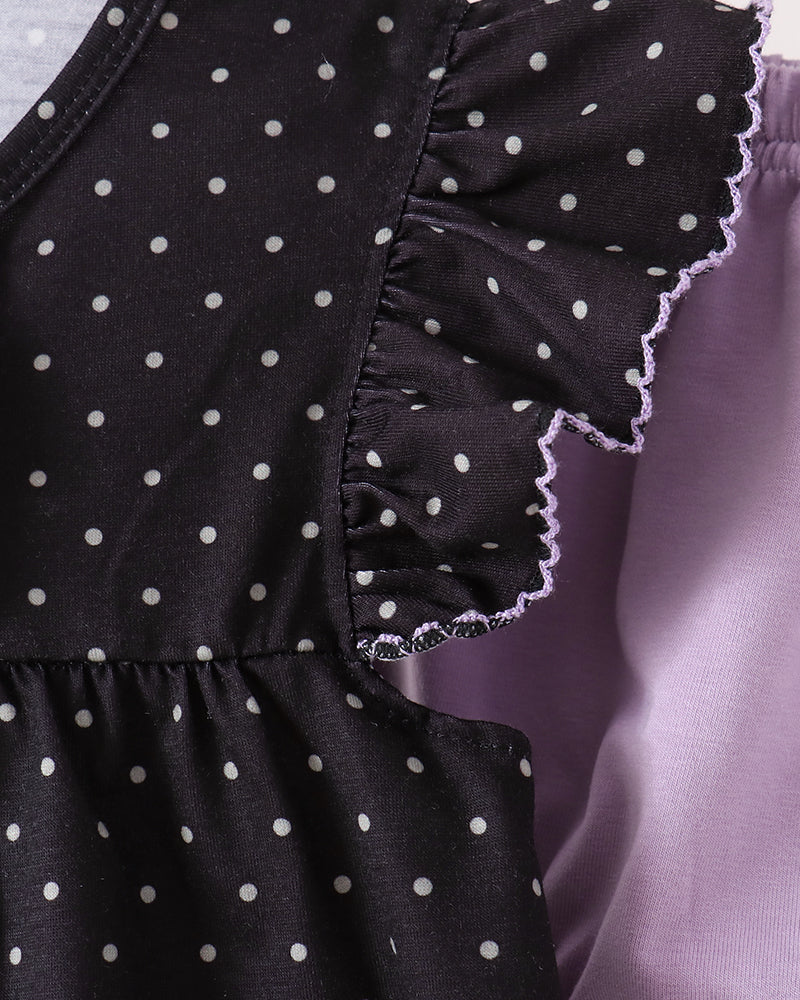 Close-up of a black top with white polka dots and ruffled sleeves, hanging on a wooden hanger next to a lavender garment.