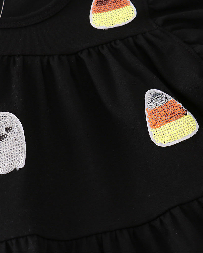 Close-up of a black ruffled garment featuring two sequined candy corn patches and part of a white sequined ghost patch on the front.