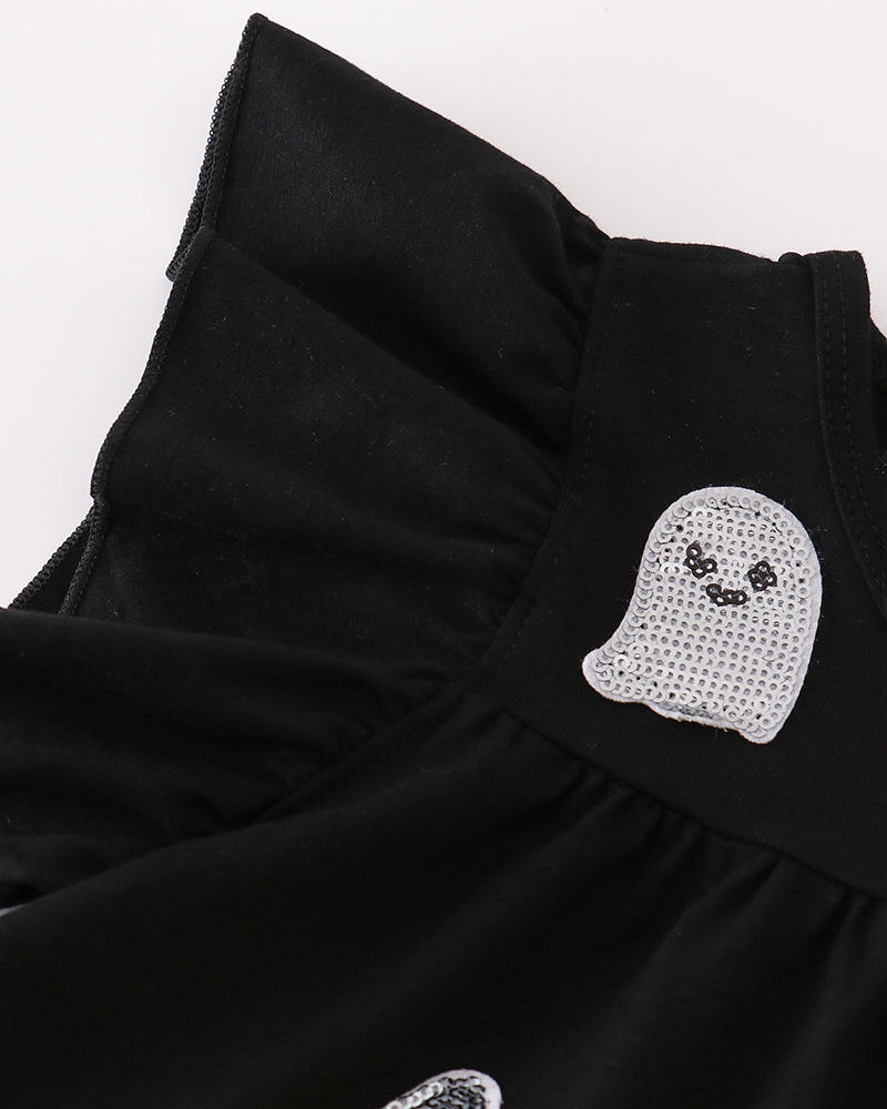 Close-up of a black ruffled garment with a ghost-shaped rhinestone patch and a candy corn patch on a white background.