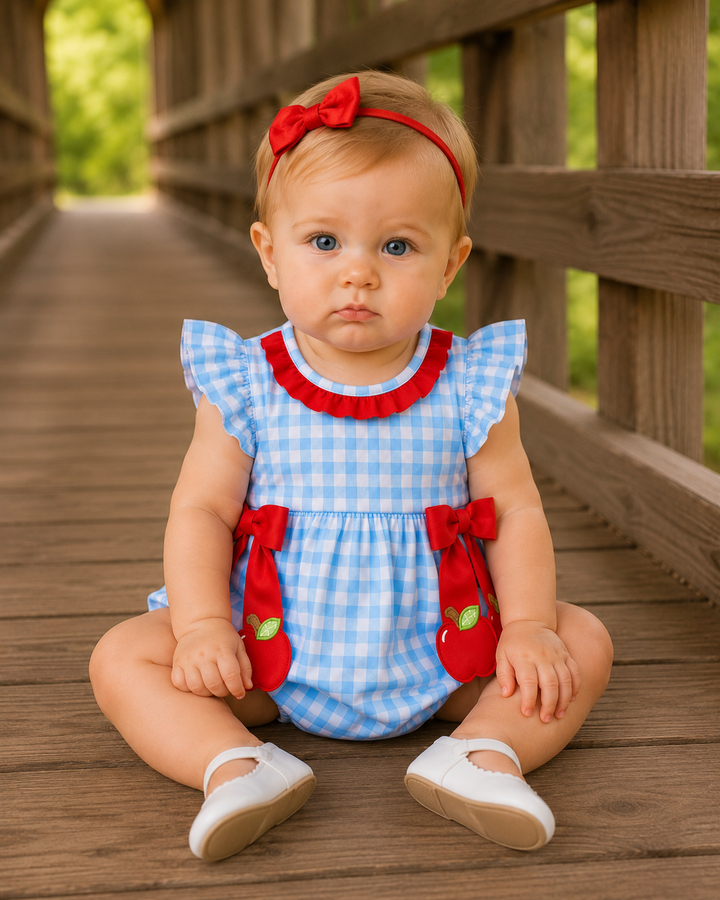 Blue gingham bubble romper with red collar and bow straps, worn by a baby