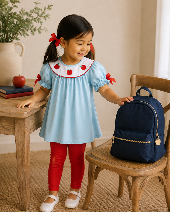 Young girl standing by table looking at a navy backpack