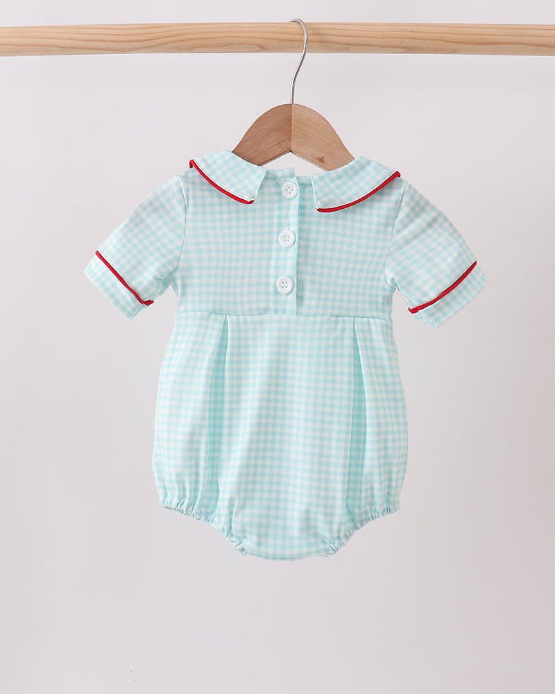Light blue checkered baby romper with red trim on a wooden hanger against a light pink background