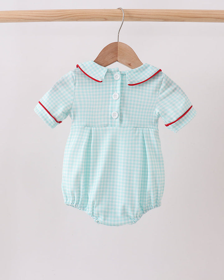 Light blue checkered baby romper with red trim on a wooden hanger against a light pink background