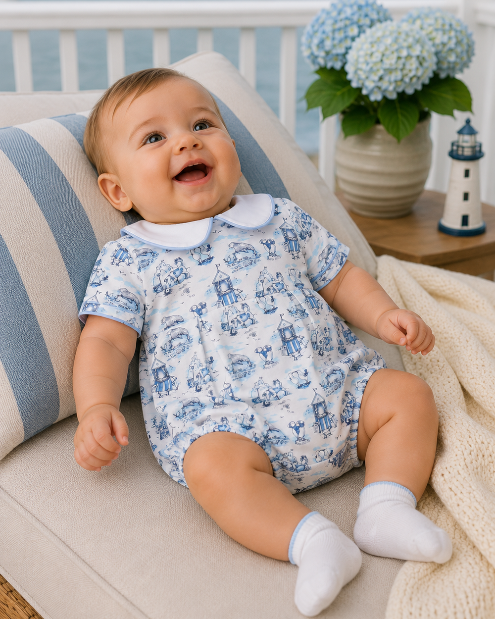 Baby in a blue and white romper sitting on a couch with a scenic background
