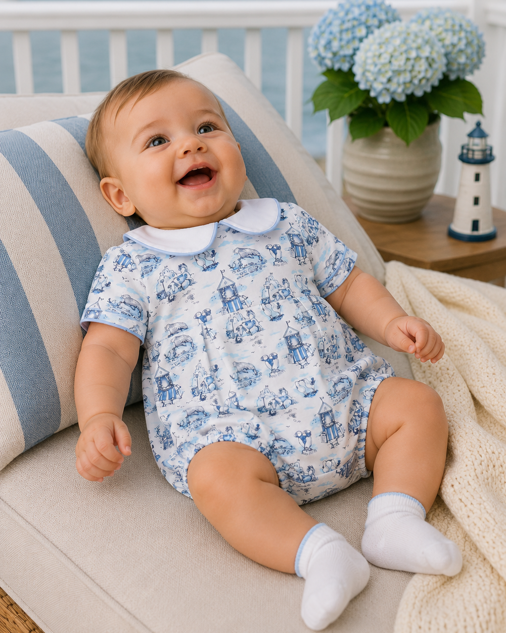 Baby in a blue and white romper sitting on a couch with a scenic background