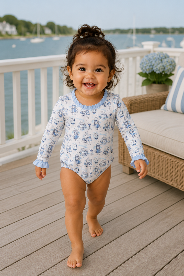 Child in a blue and white patterned swimsuit standing on a wooden deck by a waterfront.