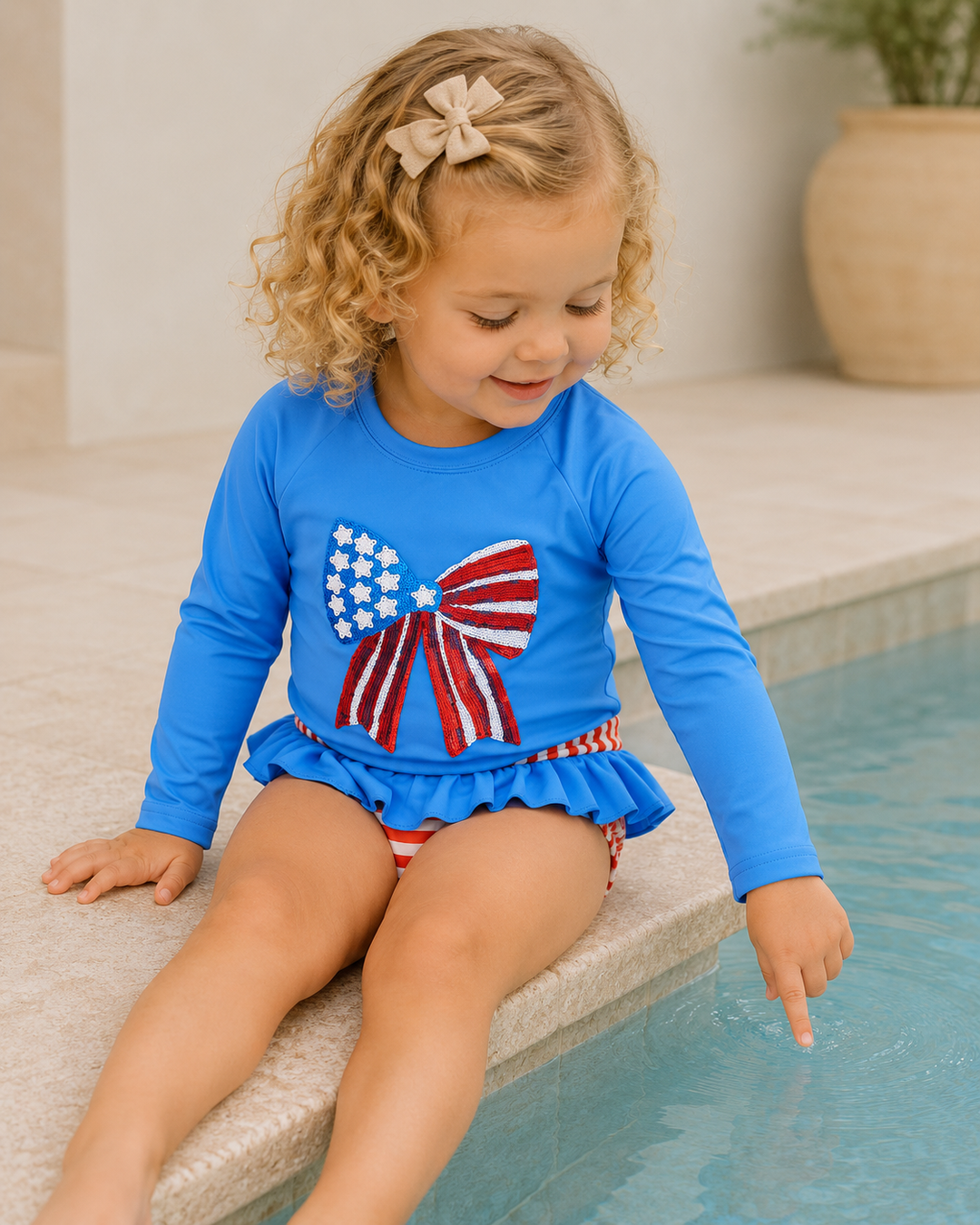 Child wearing a blue swimsuit with an American flag design, sitting by a pool.