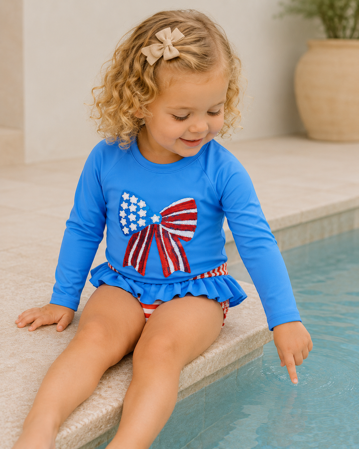 Child wearing a blue swimsuit with an American flag design, sitting by a pool.