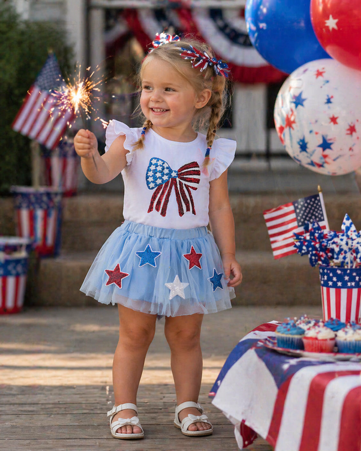 Young girl in a patriotic outfit with a sparkler, surrounded by American flags and balloons.