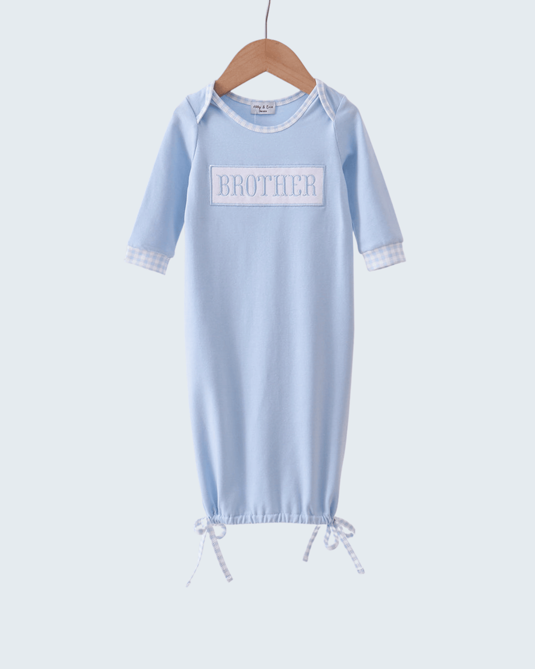 Light blue baby gown with 'BROTHER' print on a hanger against a white background