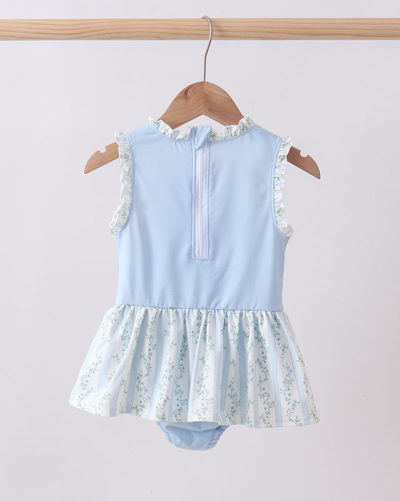 Light blue swimsuit with floral skirt on a wooden hanger against a white background