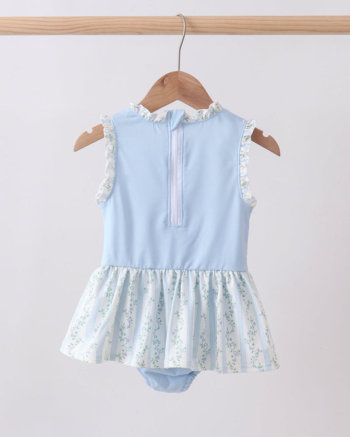Light blue swimsuit with floral skirt on a wooden hanger against a white background