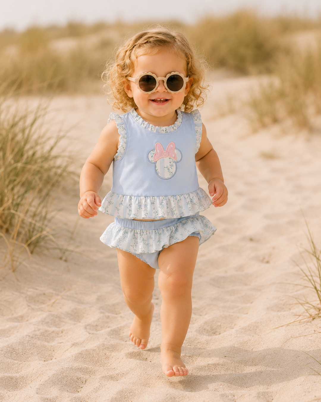 Child in light blue outfit with ruffles walking on sand