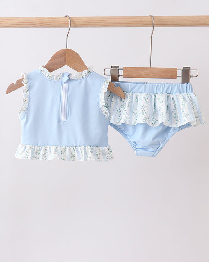 Light blue baby outfit with ruffled details on a wooden hanger against a light gray background