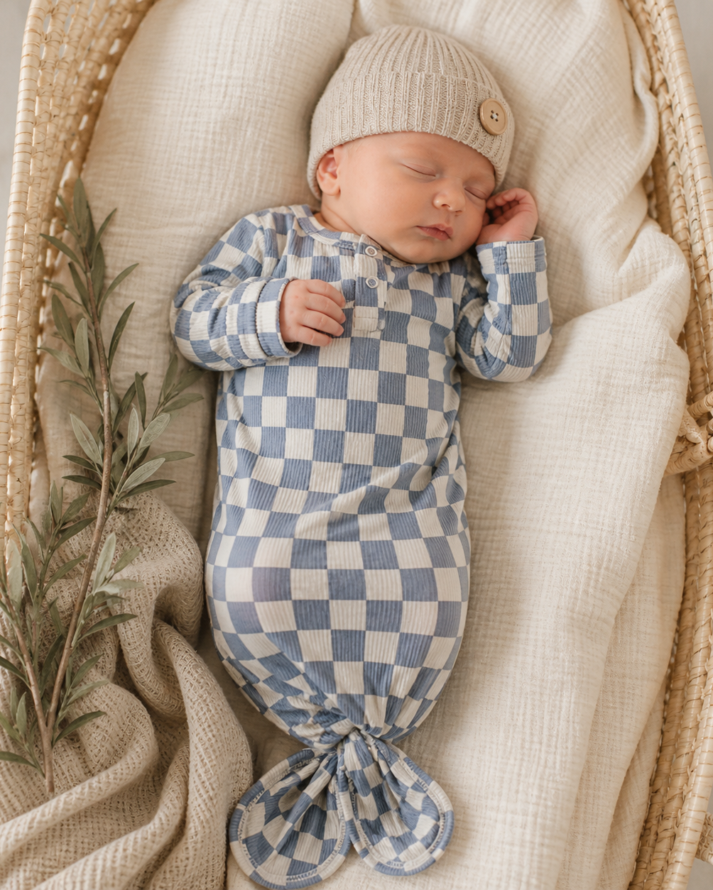 Newborn baby wrapped in a blue and white checkered swaddle, wearing a matching hat, in a wicker basket.