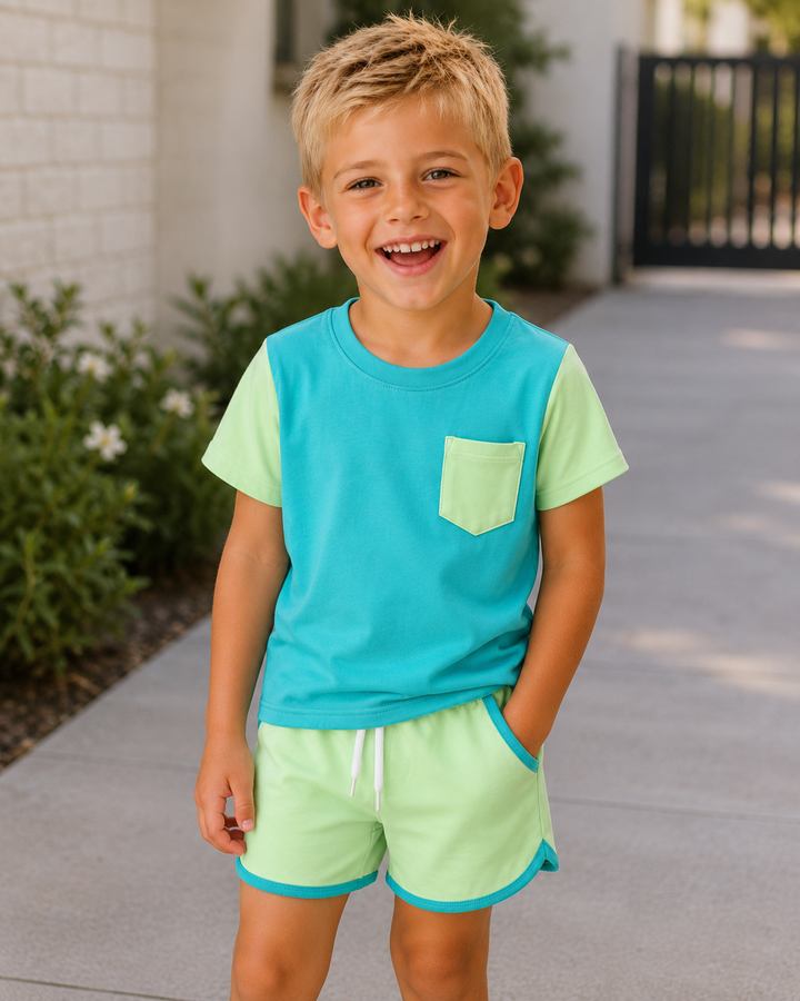 Young boy wearing a blue and green shirt and shorts set on a sidewalk.