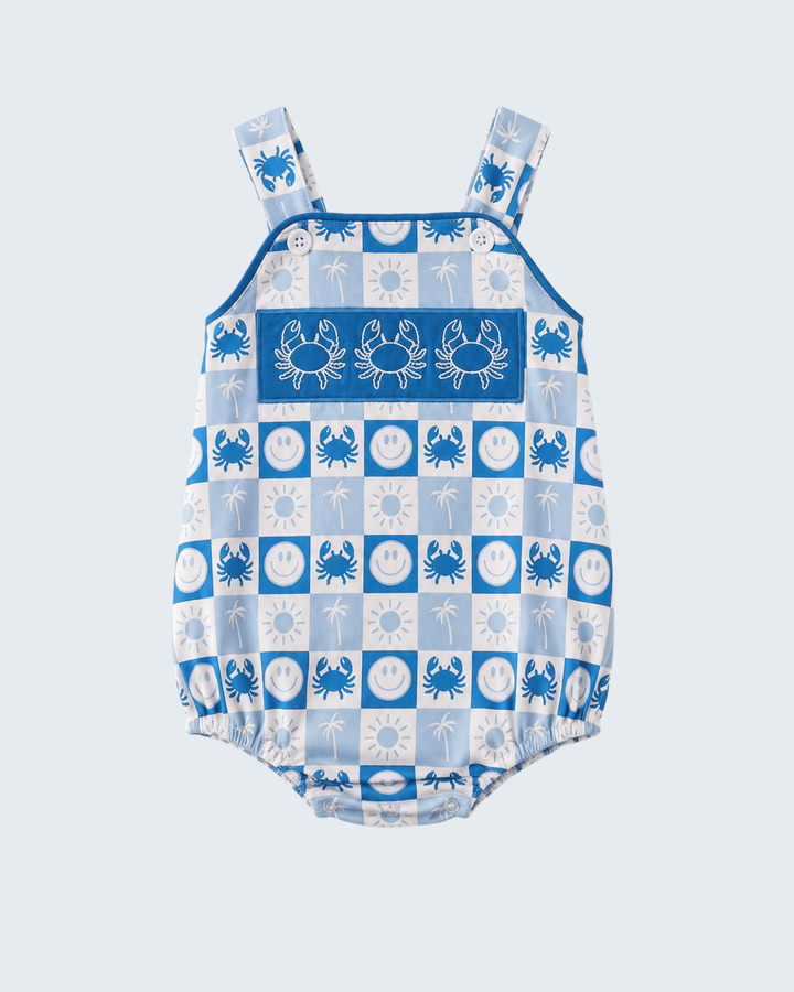A baby bubble romper with a blue and white nautical theme, featuring a checkerboard pattern of crabs, palm trees, and suns, and adjustable shoulder straps, shown against a light gray background.