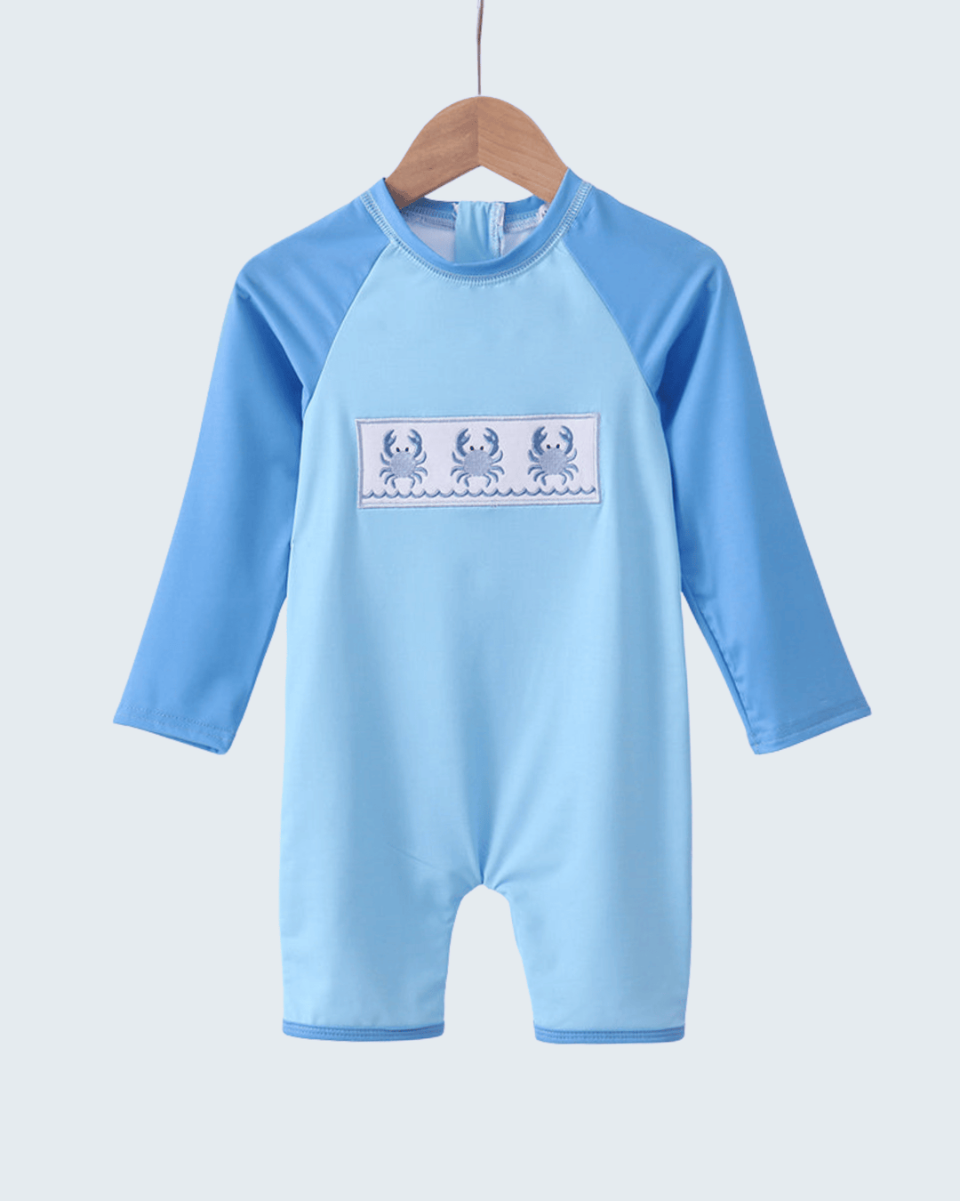 Blue children's swimsuit with long sleeves on a hanger against a light gray background