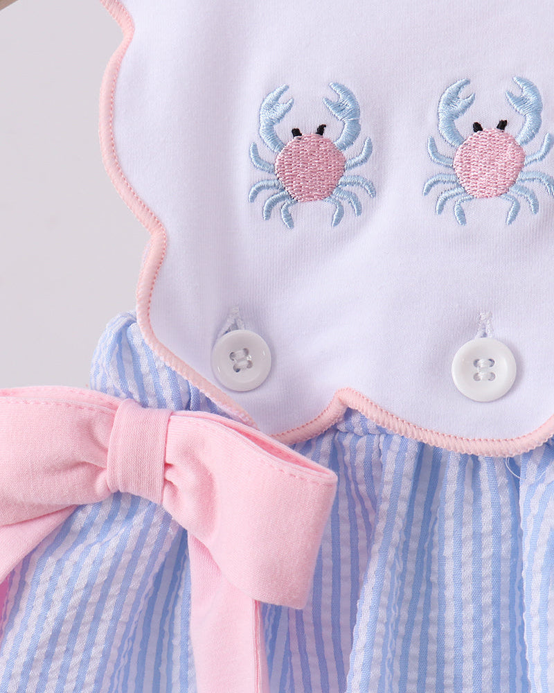 Baby dress with pink bow and crab embroidery on a light background