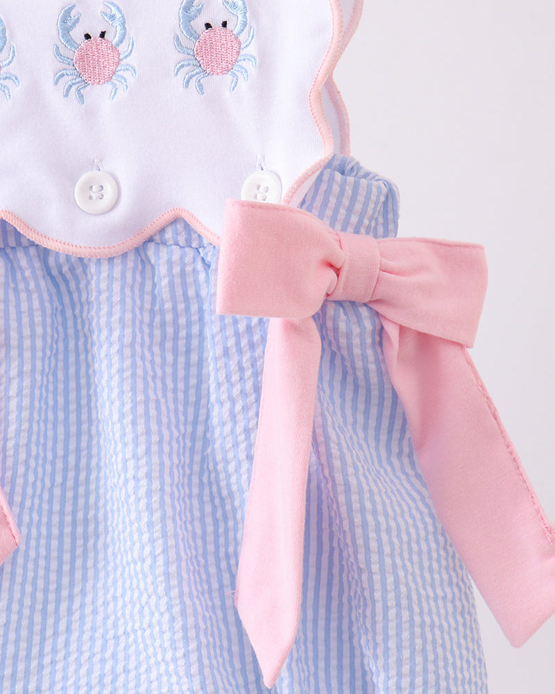 Baby romper with blue and white checkered pattern, pink bow, and crab embroidery on a white background