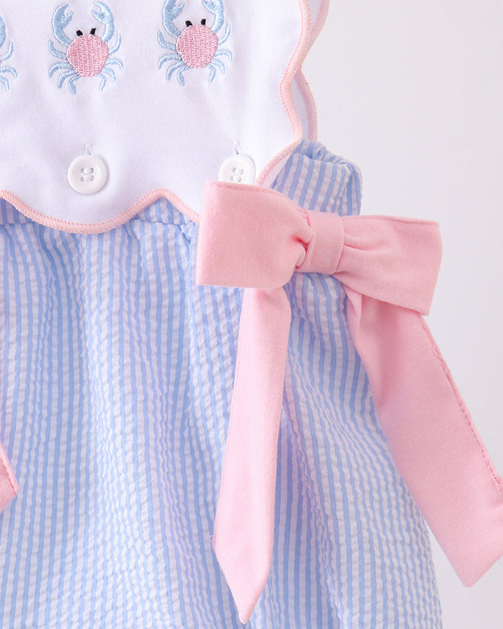 Baby romper with blue and white checkered pattern, pink bow, and crab embroidery on a white background