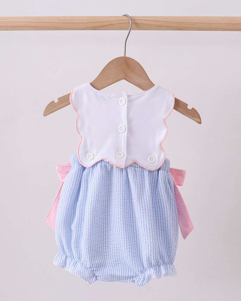 Baby romper with white top and blue checkered skirt on a hanger against a light background