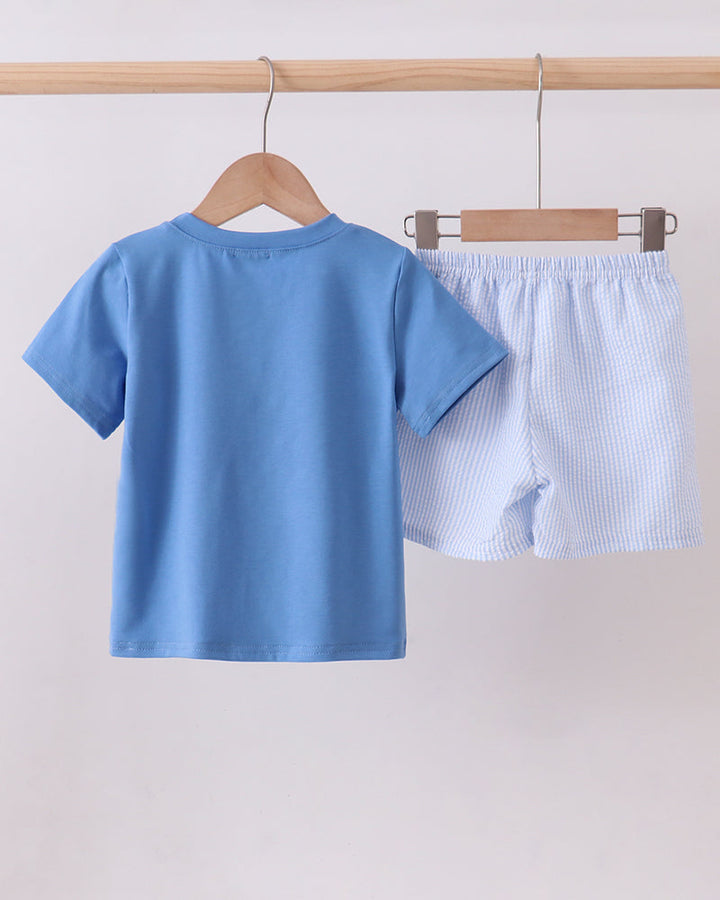 Blue t-shirt and shorts set hanging on a wooden rack against a white background