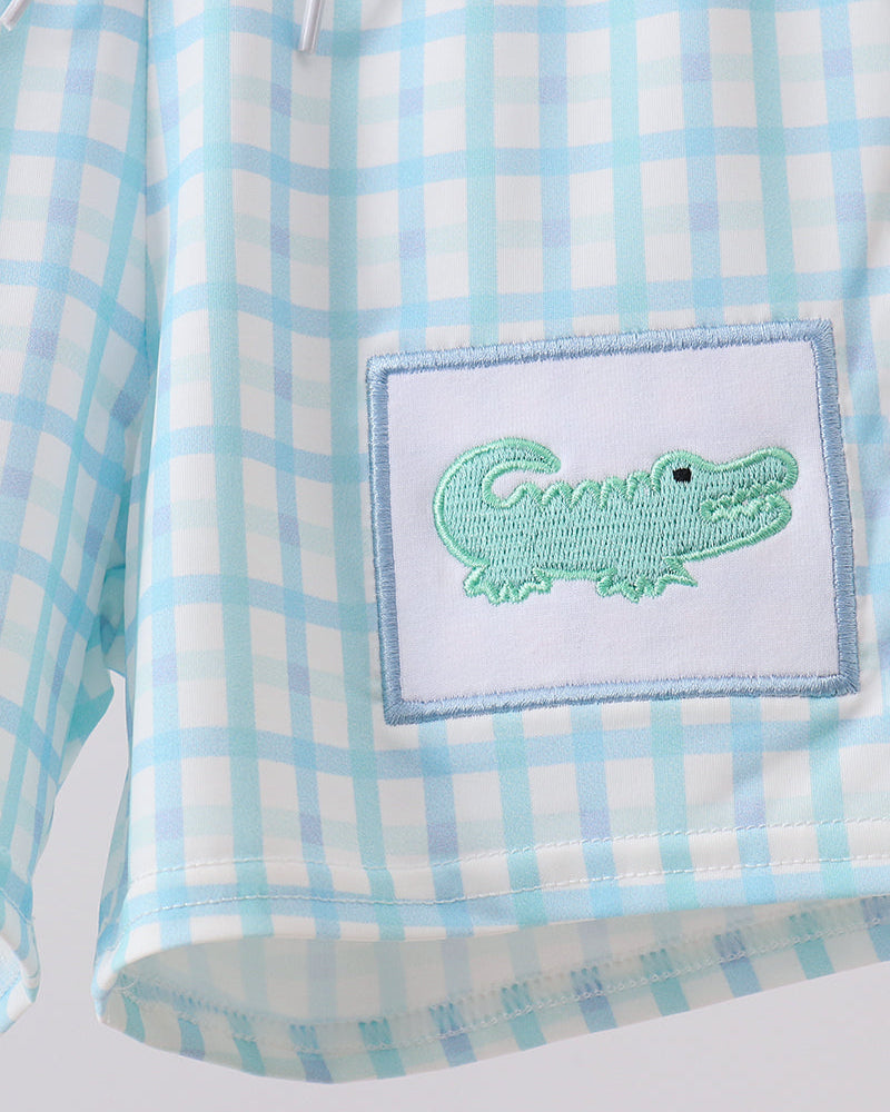 Light blue plaid swim trunks with green crocodile patch on the front pocket.