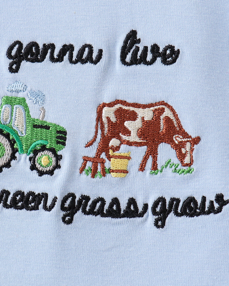 Embroidered design of a tractor and cow with text on a light blue background