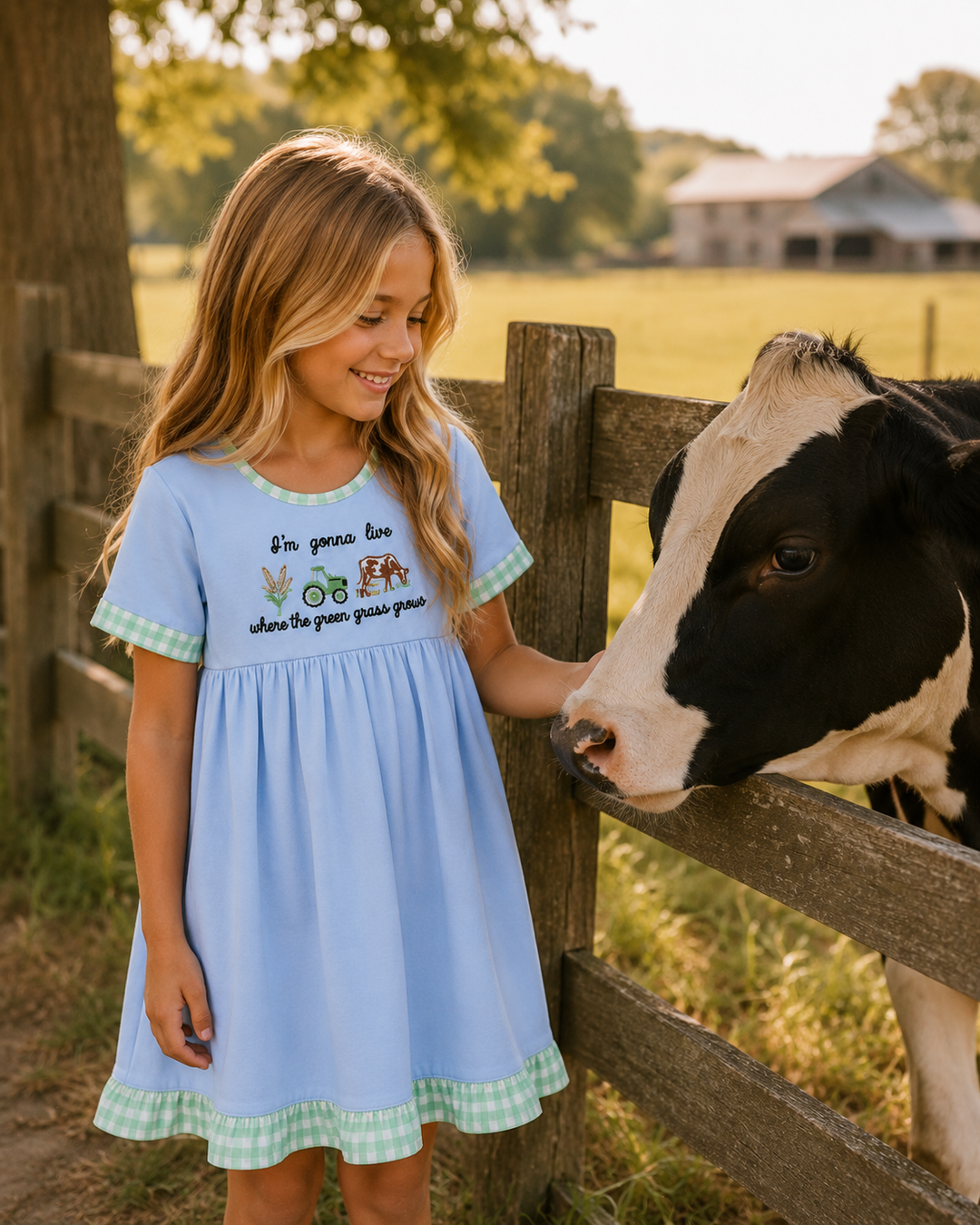 Young girl in a blue dress petting a cow through a wooden fence on a farm.
