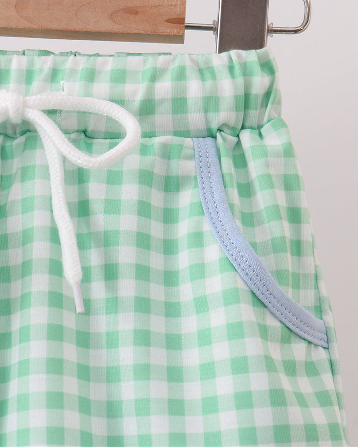 Green and white checkered shorts with a drawstring on a hanger against a white background