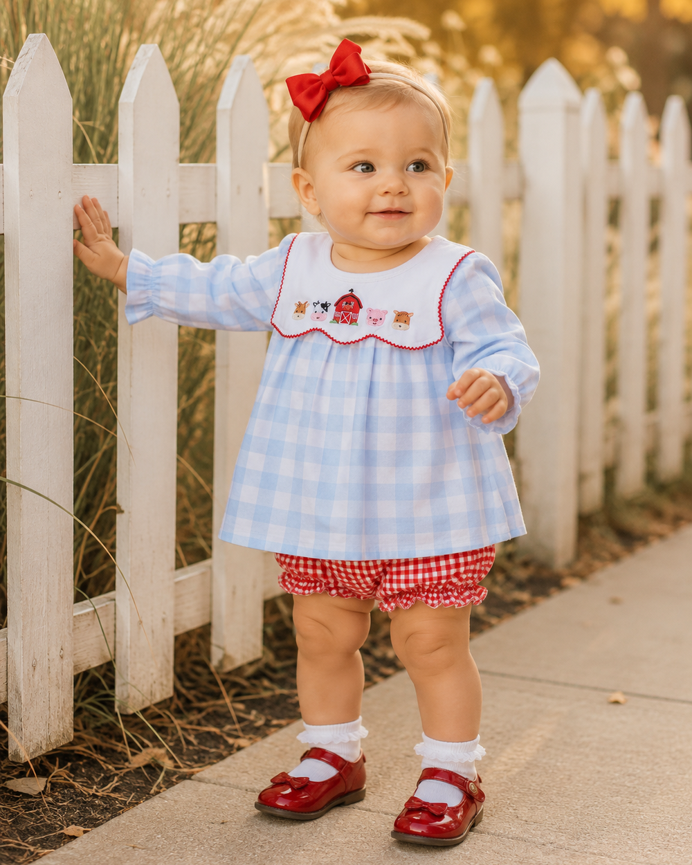 Baby wearing blue-and-white gingham dress with red trim collar and red gingham bloomer shorts
