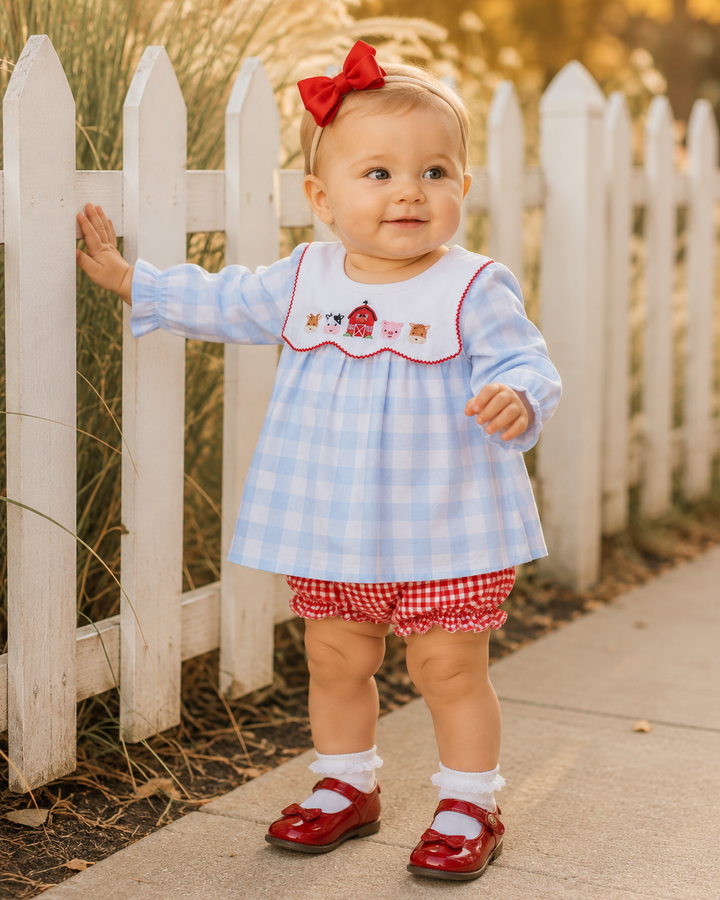 Baby wearing blue-and-white gingham dress with red trim collar and red gingham bloomer shorts
