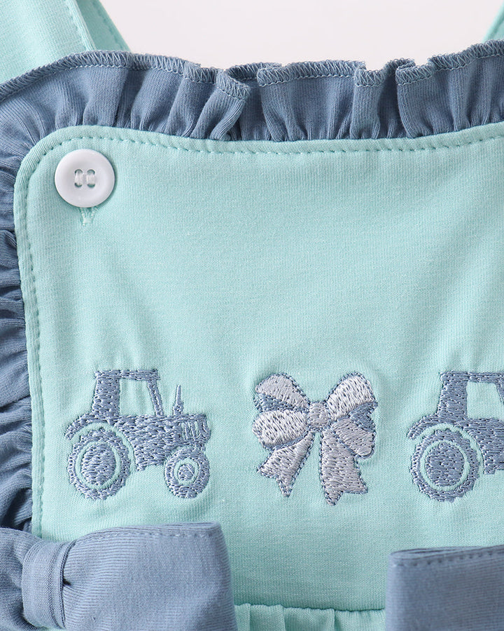 Close-up of a baby romper in mint green and dusty blue, featuring embroidered tractors and bows on the bib front panel.