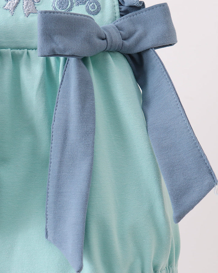 Close-up of a mint green baby romper with a dusty blue bow on the front, featuring embroidered tractors and bows on the chest.