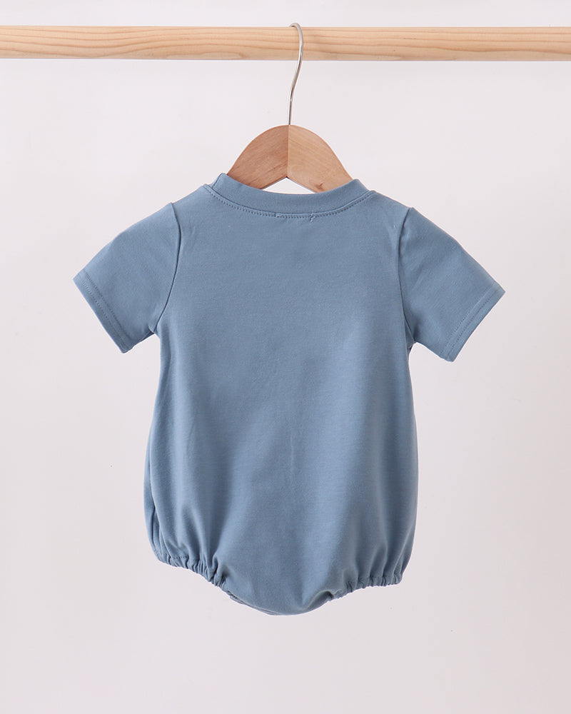 A light blue short-sleeve baby romper or bubble bodysuit hanging on a wooden hanger from a wooden clothes rack against a plain off-white background.