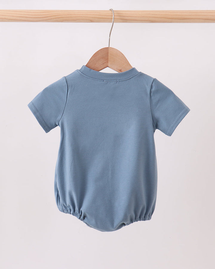 A light blue short-sleeve baby romper or bubble bodysuit hanging on a wooden hanger from a wooden clothes rack against a plain off-white background.
