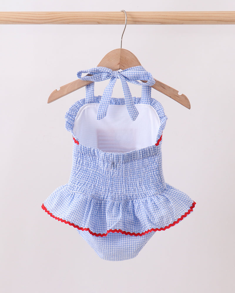Blue checkered baby swimsuit with red trim on a hanger against a white background