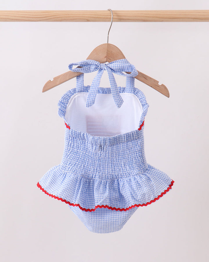 Blue checkered baby swimsuit with red trim on a hanger against a white background