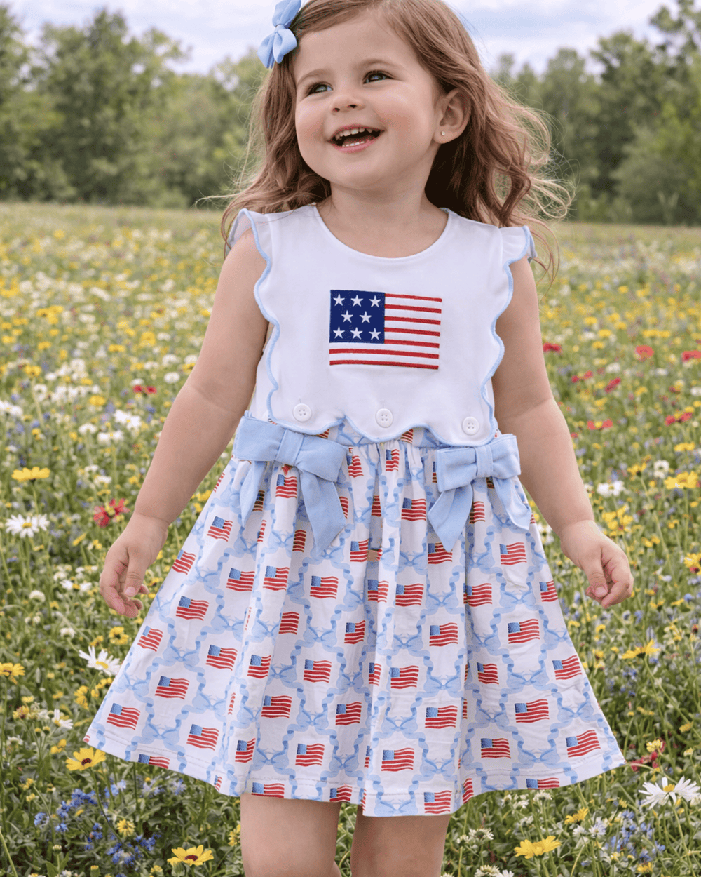 Child wearing a dress with American flag pattern in a field of flowers
