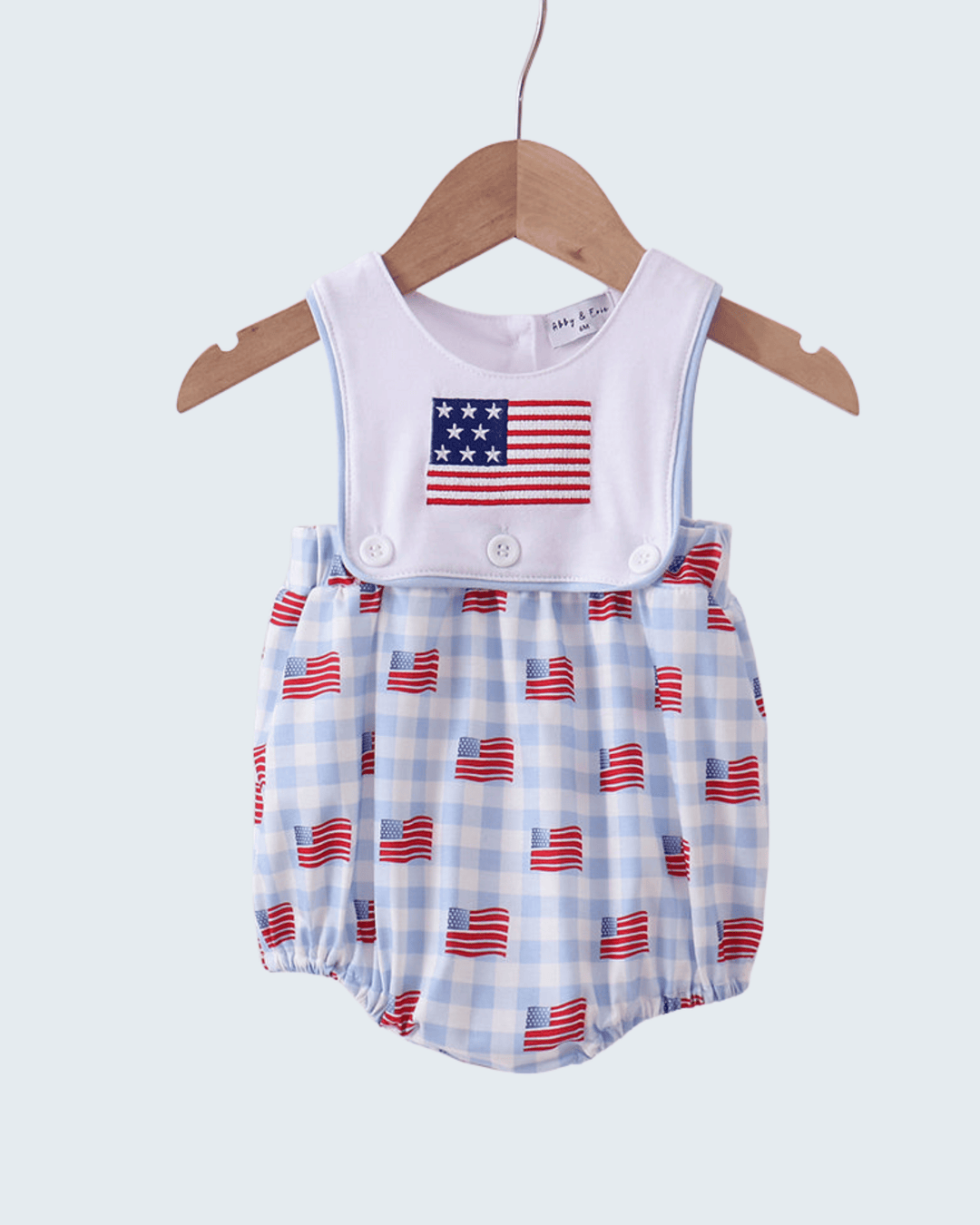 Baby romper with American flag pattern on a hanger against a light blue background