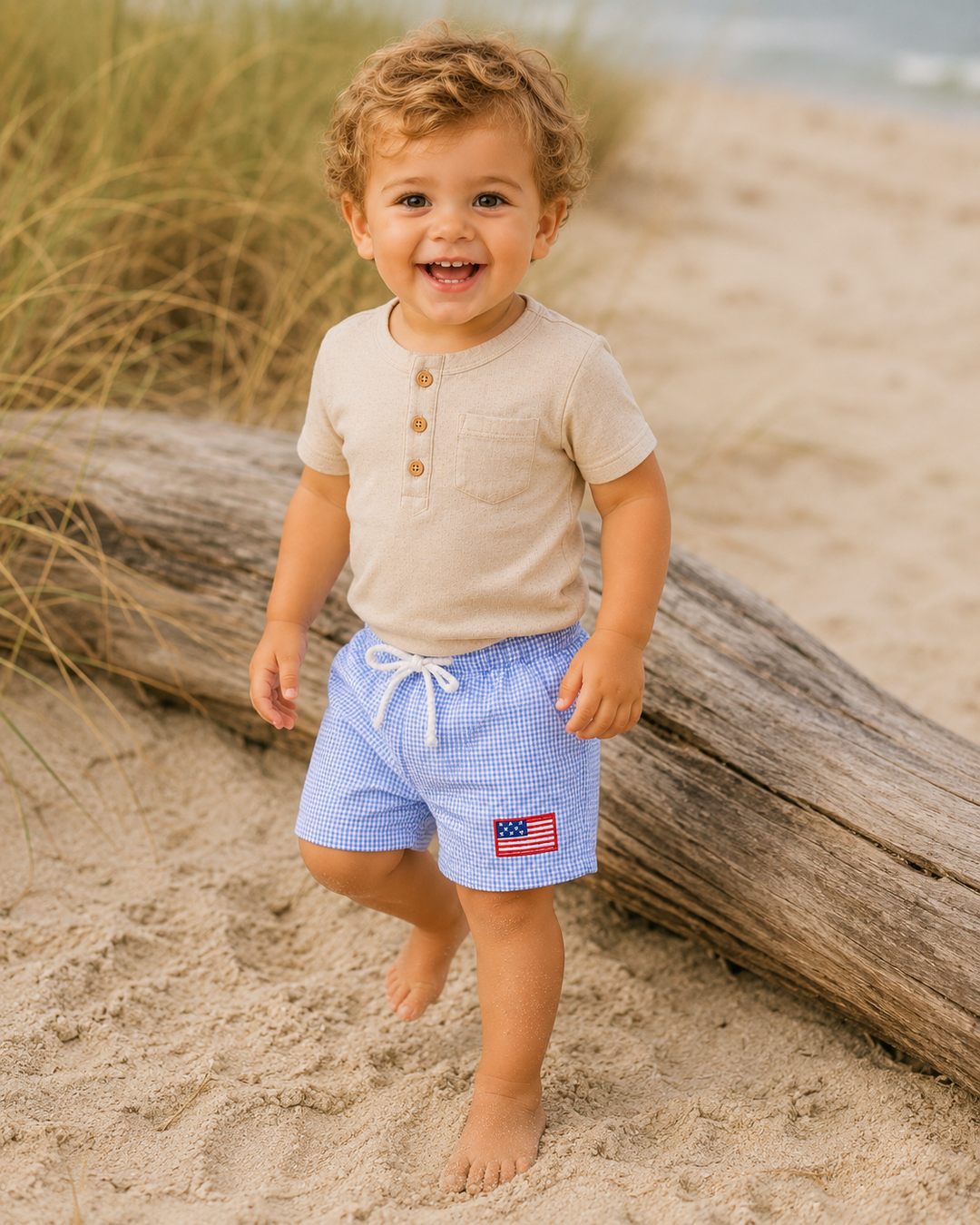 Child wearing blue checkered shorts with an American flag design on a sandy beach.
