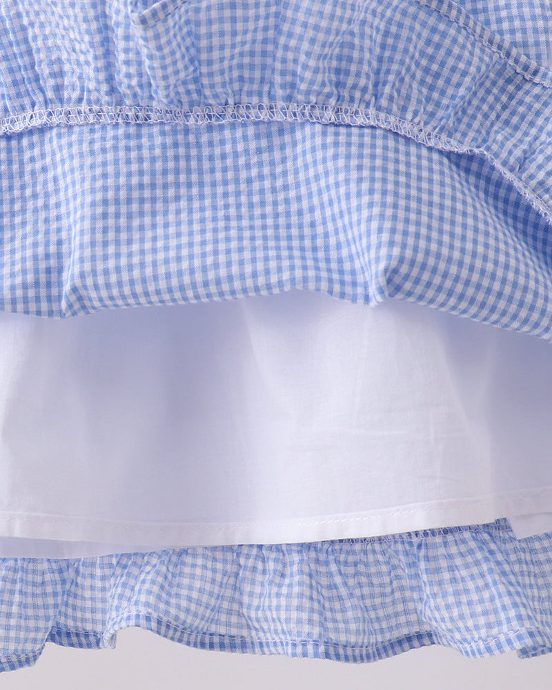 Close-up of a blue and white checkered fabric with ruffled layers on a light gray background.