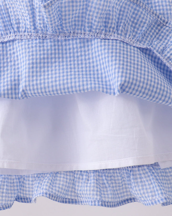 Close-up of a blue and white checkered fabric with ruffled layers on a light gray background.