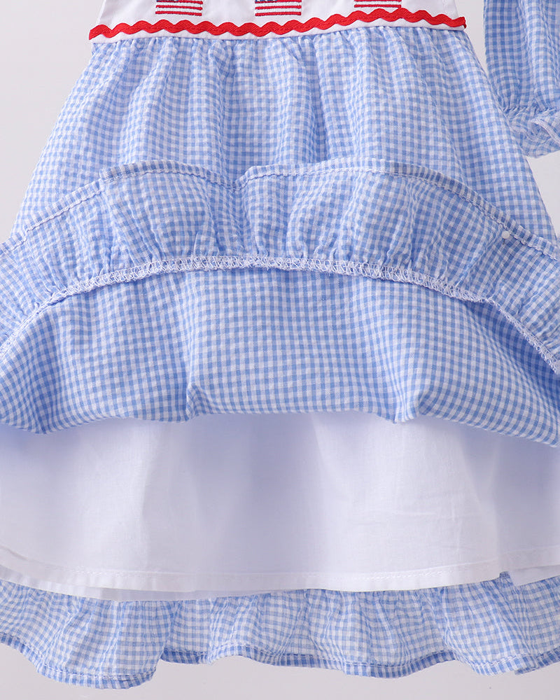 Blue checkered dress with white trim and red neckline featuring small American flags on a light gray background.