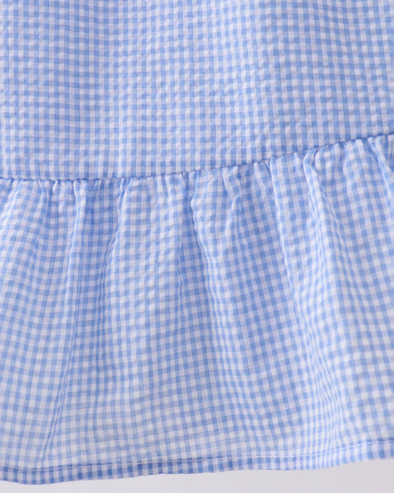 Close-up of a blue and white checkered dress with a ruffled hem on a light gray background.