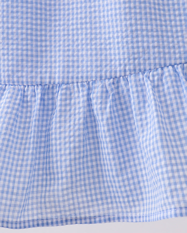 Close-up of a blue and white checkered dress with a ruffled hem on a light gray background.